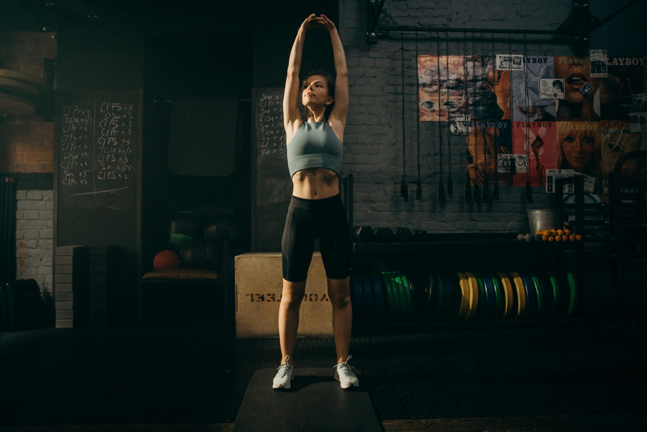 Strong woman stretching her arms in an industrial-style gym environment with motivational wall art.