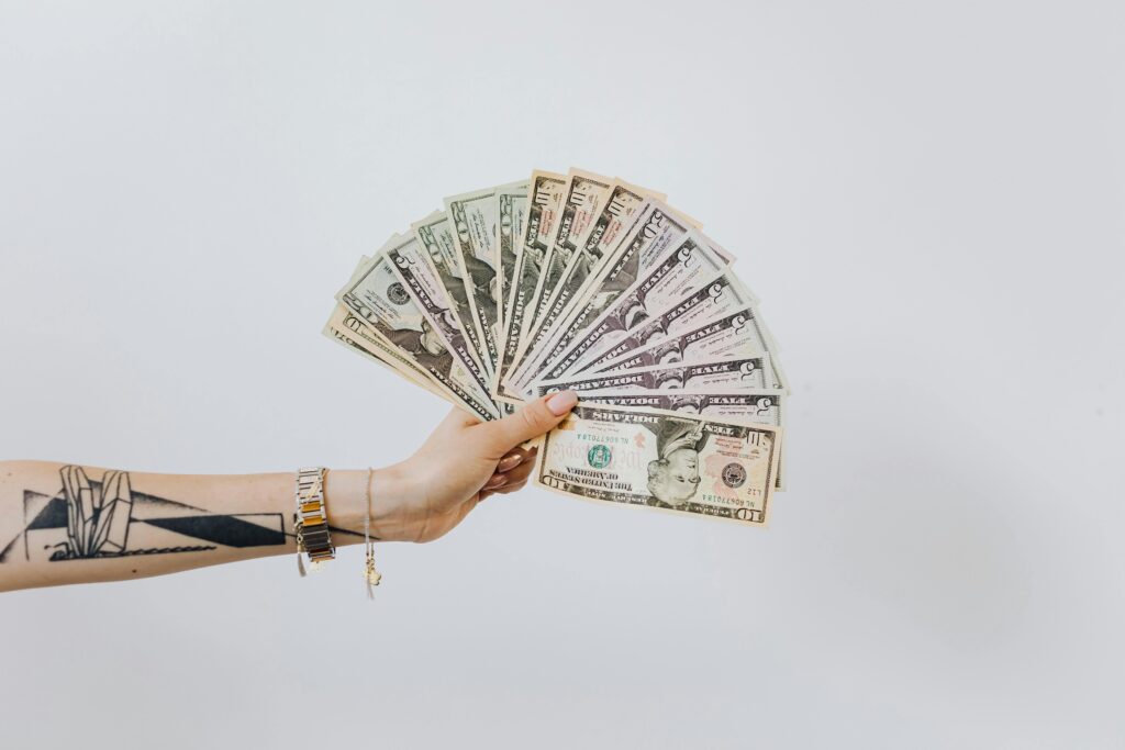 Tattooed arm holding a fan of US dollar bills on a white background, symbolizing wealth and financial success.